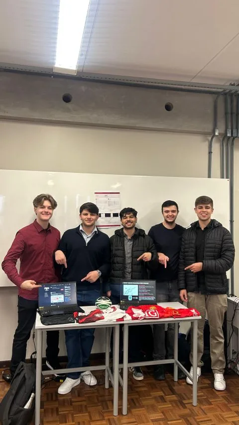 Os cinco integrantes da equipe do Draft em pé atrás de uma mesa de apresentação, apontando para dois notebooks que exibem o sistema.